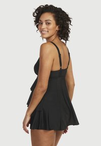 Svart simklänning med justerbara band, volangdetalj i kjolen, slätt tyg och figurnära midja, utformad för komfort och täckning.