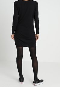 Svart långärmad klänning med figursydd silhuett, texturerad tyg och rundad halsringning. Buren med svarta strumpbyxor och avslappnade svarta skor.