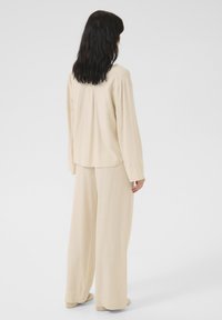 Beige långärmad skjorta med rundad nederkant, i kombination med vida byxor. Slät tyg med minimala sömmar och en avslappnad passform.