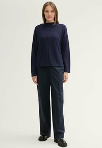 Pull en maille oversize bleu marine avec un col montant, associé à un pantalon large bleu marine et des chaussures à plateforme noires. Design simple et texturé.