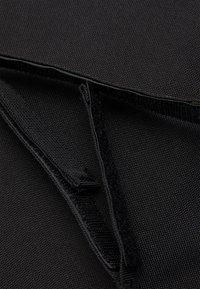 Gros plan d'un tissu noir avec des bandes Velcro qui se chevauchent et des coutures détaillées sur une surface texturée.