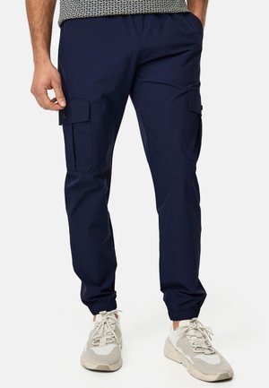 Pantalones cargo navy con bolsillos laterales, cinturilla elástica y perneras ajustadas. El material parece suave y ligero. Combinados con zapatillas de color claro.
