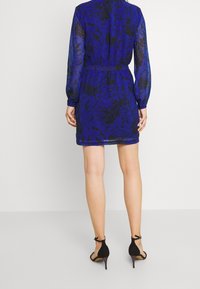 Blommig blå klänning med genomskinliga långa ärmar, åtstramad midja och knäppning bak. Bärs med svarta högklackade sandaler.