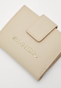 Valkoinen teksturoiduista nahasta valmistettu lompakko, jossa on magneettinen läppä ja kohokuvioitu kultainen "VALENTINO" -logo etuosassa. Kompakti suorakulmainen muoto.