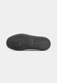 Semelle de chaussure en caoutchouc noir avec des motifs de bande de roulement circulaires et linéaires, avec le logo Puma au centre.