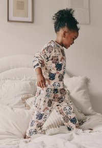 Set di pigiami per bambini in morbido tessuto beige, caratterizzato da una stampa giocosa di vari animali dei cartoni animati e arcobaleni. Include maniche lunghe e pantaloni.