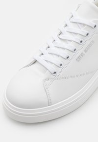 Sneaker alb din piele cu vârful rotunjit, șireturi albe plate și detalii de cusătură subtile. Prezintă logo-ul "Steve Madden" gravat pe lateral.
