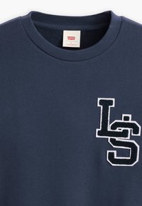 Marineblauwe trui met ronde hals, gemaakt van zacht materiaal, met een textuur van een witte en donkerblauwe geborduurde "LS"-logo op de linkerkant van de borst.