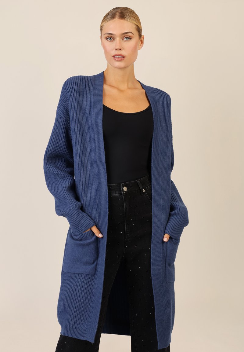 Pitkä, avonainen etukardigan syvänsinisestä neuleesta, jossa ribbikuvio, leveät hihat, kaksi etutaskua ja rento istuvuus.