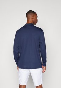 Långärmad polo-shirt i marinblått, tillverkad av mjukt tyg. Har en klassisk krage, åtsittande design och diskreta sömnadsdetaljer på axlarna.