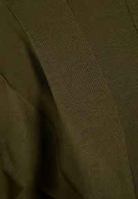 Gros plan sur un tissu tricoté vert olive avec des textures côtelées et gaufrées variées créant un motif de lignes diagonales et verticales.