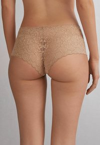 Nude koronkowe majtki typu boyshort, ozdobione kwiatowymi wzorami i falbaniastym wykończeniem. Miękka tekstura i średni stan, zaprojektowane z myślą o komforcie.