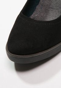 Černé semišové baleríny s špičatou špičkou, příjemnou texturou a nízkou černou gumovou podrážkou. Vnitřní podšívka vypadá měkce a má mírně texturovaný povrch.