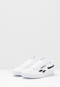 Weiße Leder-Sneaker mit perforierter Zehenpartie, schwarzen Seitenstreifen und einer weißen Gummisohle. Enthält Logo-Details auf der Zunge.