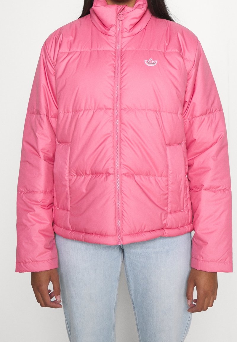 Rosa puffjacka med hög krage, horisontell quiltad design och en liten vit logotyp på vänster bröst. Har sidofickor.