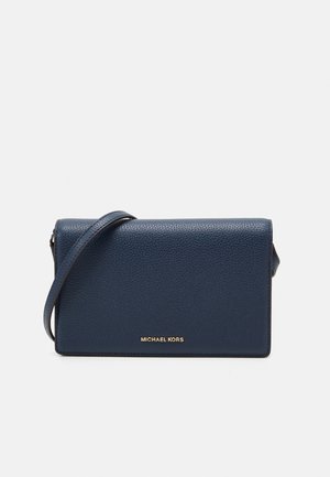 Granatowa skórzana torebka na ramię Michael Kors z ziarnistą fakturą i cienkim paskiem, pokazana na jednolitym jasnym tle.