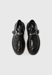 Sorte skinnsko med spenne og sølvhardware. Tekst "VALENTINO" på spennen. Tykke sorte såler, glatt tekstur, rund form.
