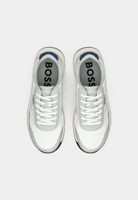 Fehér sportcipők sima bőr felsőrésszel, szürke részletekkel, kék díszítéssel a saroknál és fehér fűzőkkel. Texturált talppal rendelkeznek.