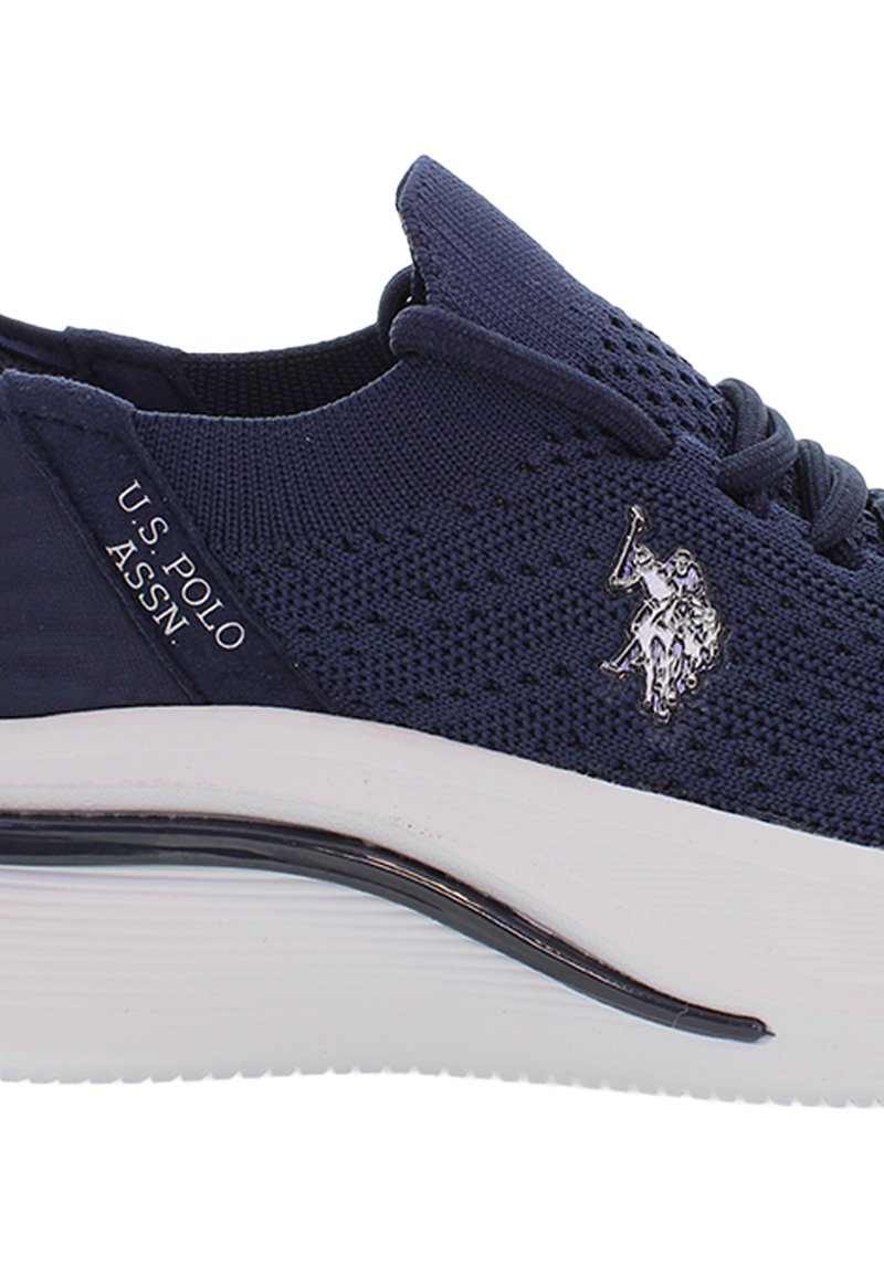 Zapatilla de punto en color navy con un diseño elegante, que cuenta con una suela blanca y un acento de logo plateado. Textura transpirable y cierre de cordones.