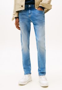 Jasnoniebieskie dżinsy o dopasowanym kroju, z subtelnym blaknięciem, tradycyjnym fasonem z pięcioma kieszeniami, zestawione z białymi trampkami.