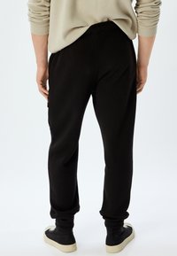 Sorte joggerbukser lavet af blødt stof, med en tapered benform, elastiske manchetter og en baglomme med lynlåsdetalje.
