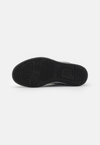 Black rubber sole with textured tread pattern, featuring circular and hexagonal grips; smooth edge and prominent logo detail.