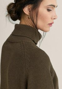 Brun strikket sweater med høj ribstrikket krave, med et tekstureret mønster langs skuldrene og en glat finish på kroppen.