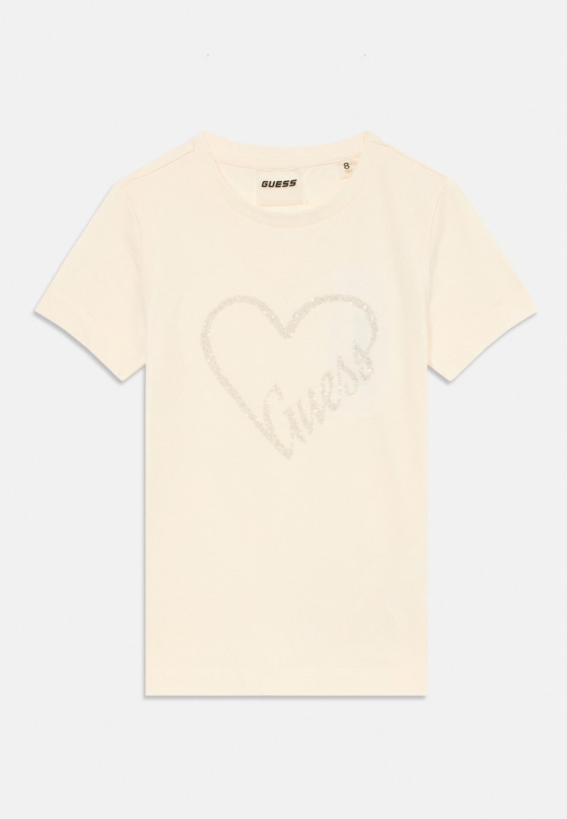 Krēmkrāsas kokvilnas t-krekls ar spīdīgu sirds dizainu, kurā iekšā ir vārds "Guess", īsām piedurknēm un apaļo kakla izgriezumu.