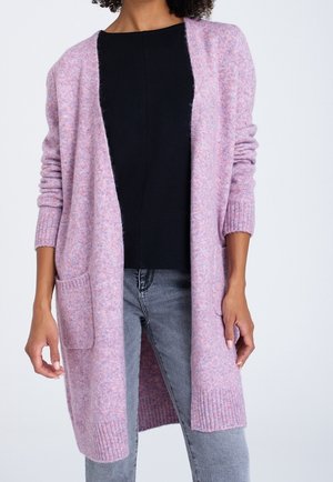 Donna che indossa un lungo cardigan rosa aperto sul davanti con tasche, top nero e jeans grigi, mostrata dalle spalle a metà coscia.