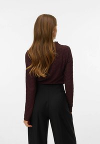 Vinröd tröja med långa ärmar och texturerat mönster, kombinerad med högmidjade svarta byxor. Mjukt tyg och figurnära silhuett framhäver designen.