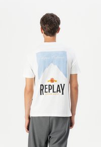 Hvit bomull T-skjorte med et fjellmotiv med teksten "Aspen Colorado" over og "REPLAY GRAND HOTEL" logo under i svart og rødt.