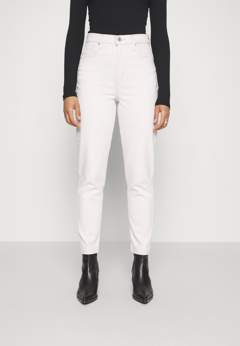 Jean blanche taille haute en denim, avec une coupe ajustée, des poches avant et une fermeture à boutons, associé à des bottines noires.