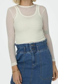 Top a maniche lunghe bianco a coste indossato sotto una canotta color crema, abbinato a una gonna in denim a vita alta con cintura arricciata e dettaglio dei bottoni.