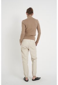 Langärmliges, figurbetontes Oberteil in Hellbraun, kombiniert mit taillierten, cremefarbenen Hosen mit elastischen Bündchen und schwarzen Slippern.