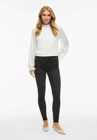 Witte textuur langekuit top met een aansluitende halslijn, gecombineerd met slim zwarte jeans en lichtbeige puntige schoenen.