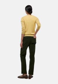 Pull en laine jaune avec poignets côtelés, pantalon en velours côtelé vert et mocassins tissés marron. Vue de dos mettant en valeur les textures de la tenue.