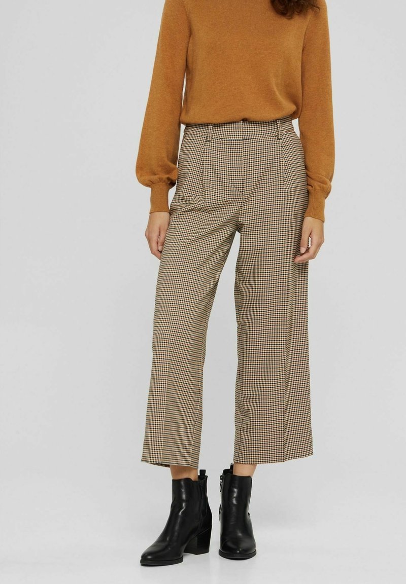 Bruna rutiga byxor med hög midja och vida ben, kombinerade med en åtsittande rustfärgade tröja och svarta ankelstövlar.