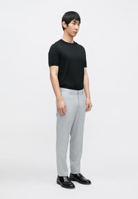 Juoda trumpomis rankovėmis marškinėliai derinami su šviesiai pilkomis kelnėmis, pasižyminčiomis lygiu audiniu ir pritaikyta siuvimo linija, papildyti juodais slip-on batais.