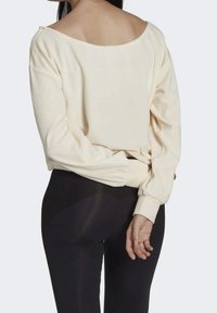 Krämfärgad långärmad topp med off-shoulder-design, ribbade ärmslut och avslappnad passform, tillsammans med svarta leggings. Mjuk tygkvalitet.