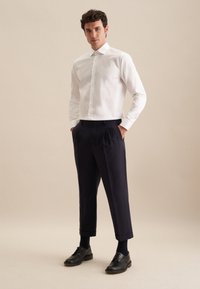 Witte knopshirt, marineblauwe geplooide broek, zwarte schoenen, met een getailleerde pasvorm. Vloeiende stofstructuur, nauwkeurige ontwerpeisen en broek tot op de enkel.