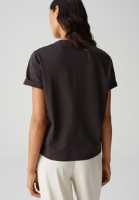Zwarte katoenen T-shirt met opgerolde korte mouwen en een ronde zoom, van achteren gezien, met een gladde textuur en een minimalistisch ontwerp.