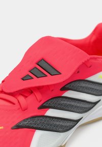 Scarpe da atletica rosse con una parte superiore testurizzata, accenti neri, lacci sottili e una suola flessibile con un battistrada a motivo.