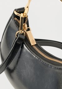 Μαύρη δερμάτινη τσάντα χειρός με χρυσλό φερμουάρ και αντίστοιχο χρυσό μεταλλικό στοιχείο στο λουράκι, σε κοντινή λεπτομέρεια.