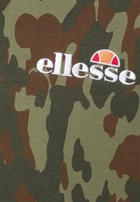 Materiał w wzór moro w zielonych i brązowych tonach, z wyhaftowanym białym logo "ellesse" oraz czerwono-pomarańczowym akcentem nad nim.