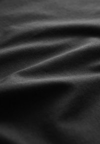 Soepel zwart stof met zachte plooien en subtiele textuur, verlicht door zacht licht.