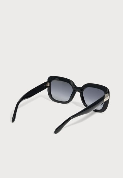 Lunettes de soleil rectangulaires noires avec verres dégradés foncés et branches fines incurvées sur un fond clair uni.
