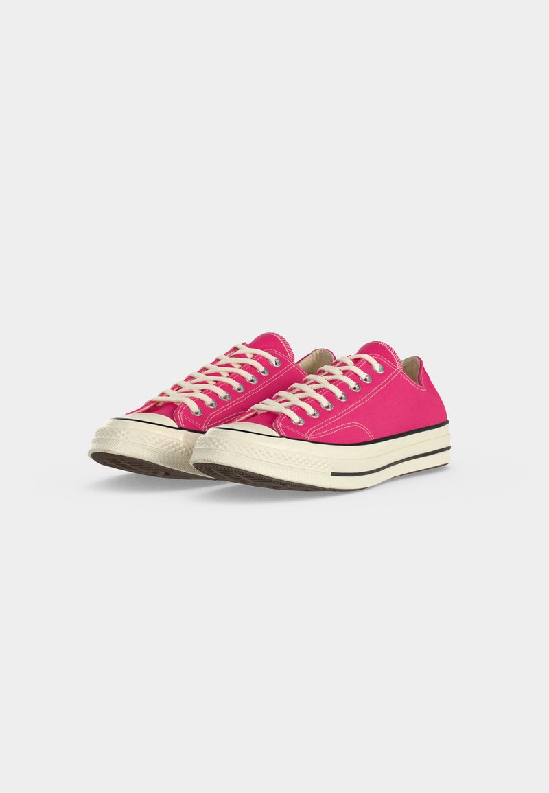 Paar niedrig geschnittene, leuchtend pinke Canvas-Sneaker mit weißen Schnürsenkeln, dicken weißen Gummisohlen und schwarzem Rand auf weißem Hintergrund.