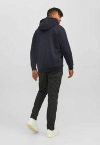 Marinefarbener Kapuzenpullover mit lockerer Passform, gerippten Bündchen und Saum; kombiniert mit dunklen Cargo-Hosen und weißen Turnschuhen.