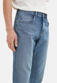 Jeans din denim bleu deschis, cu croială dreaptă, design cu cinci buzunare și cusături contrastante. Textură netedă cu detalii minime de uzură.