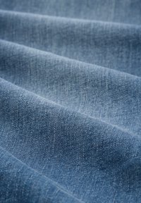 Tela de denim en azul claro, con un tejido de sarga. La superficie muestra una textura sutil con tonos variados y hilos finos y uniformes.